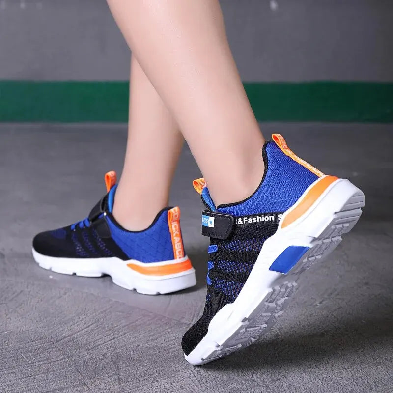 Blue and black sneakers with orange accents worn by a person on a gray floor.
