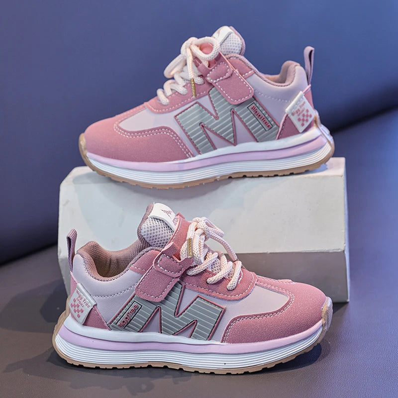 Pair of pink and gray children's sneakers on a white block against a blue background